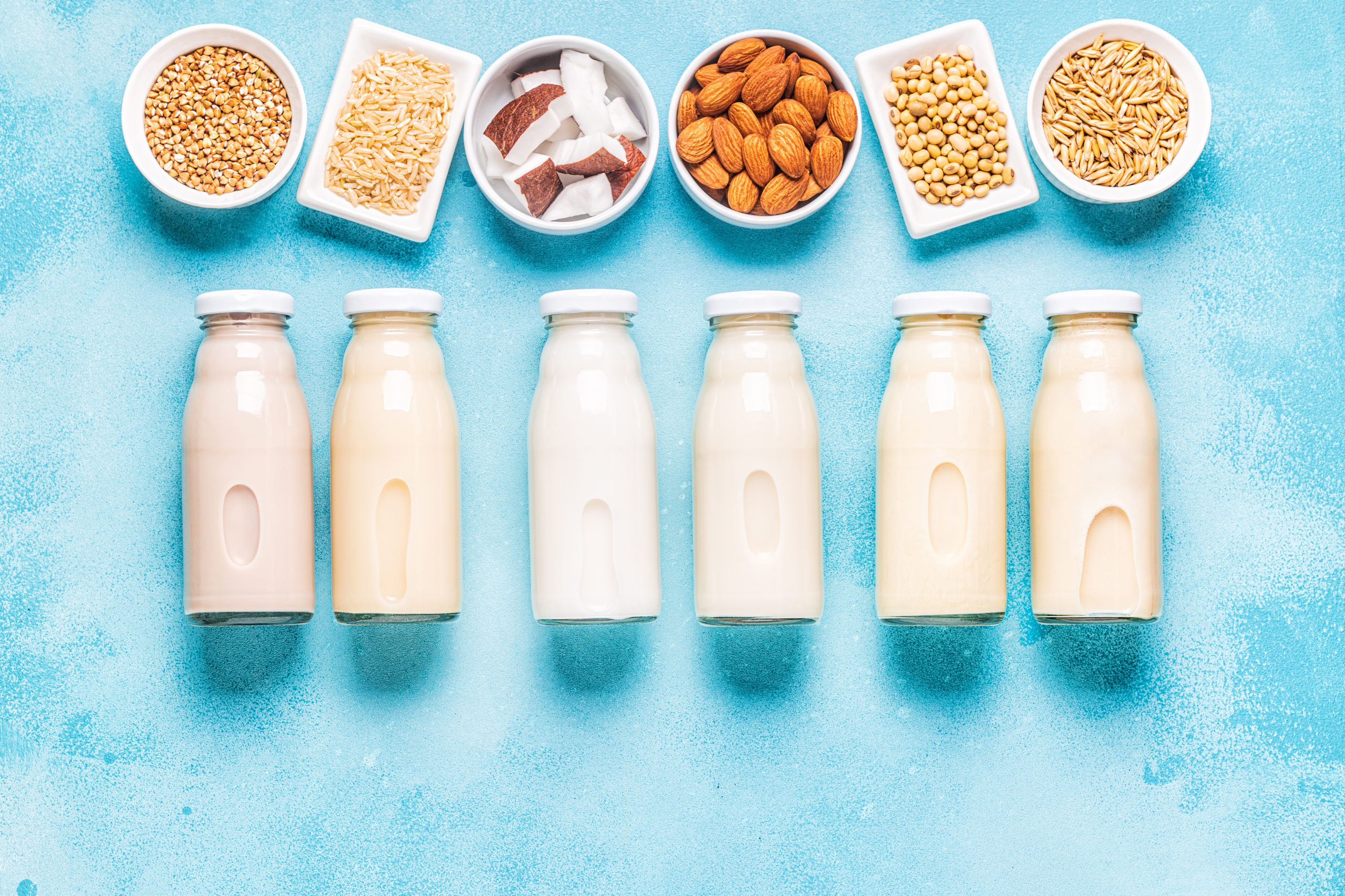 Bottles of dairy-free milk and ingredients including oats, almonds, and coconut.