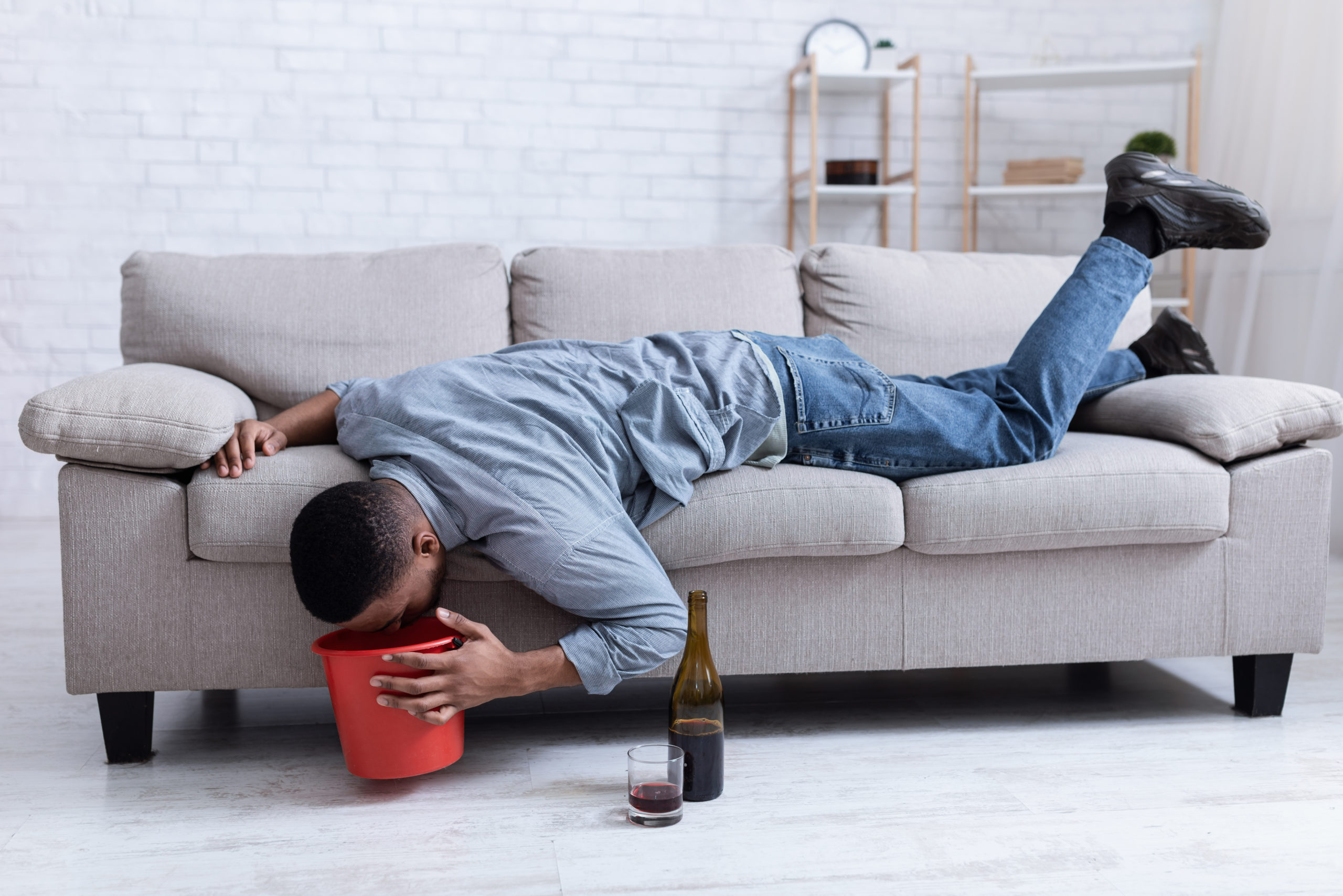 Man vomiting into bucket after drinking wine, illustrating alcohol poisoning and binge drinking effects.
