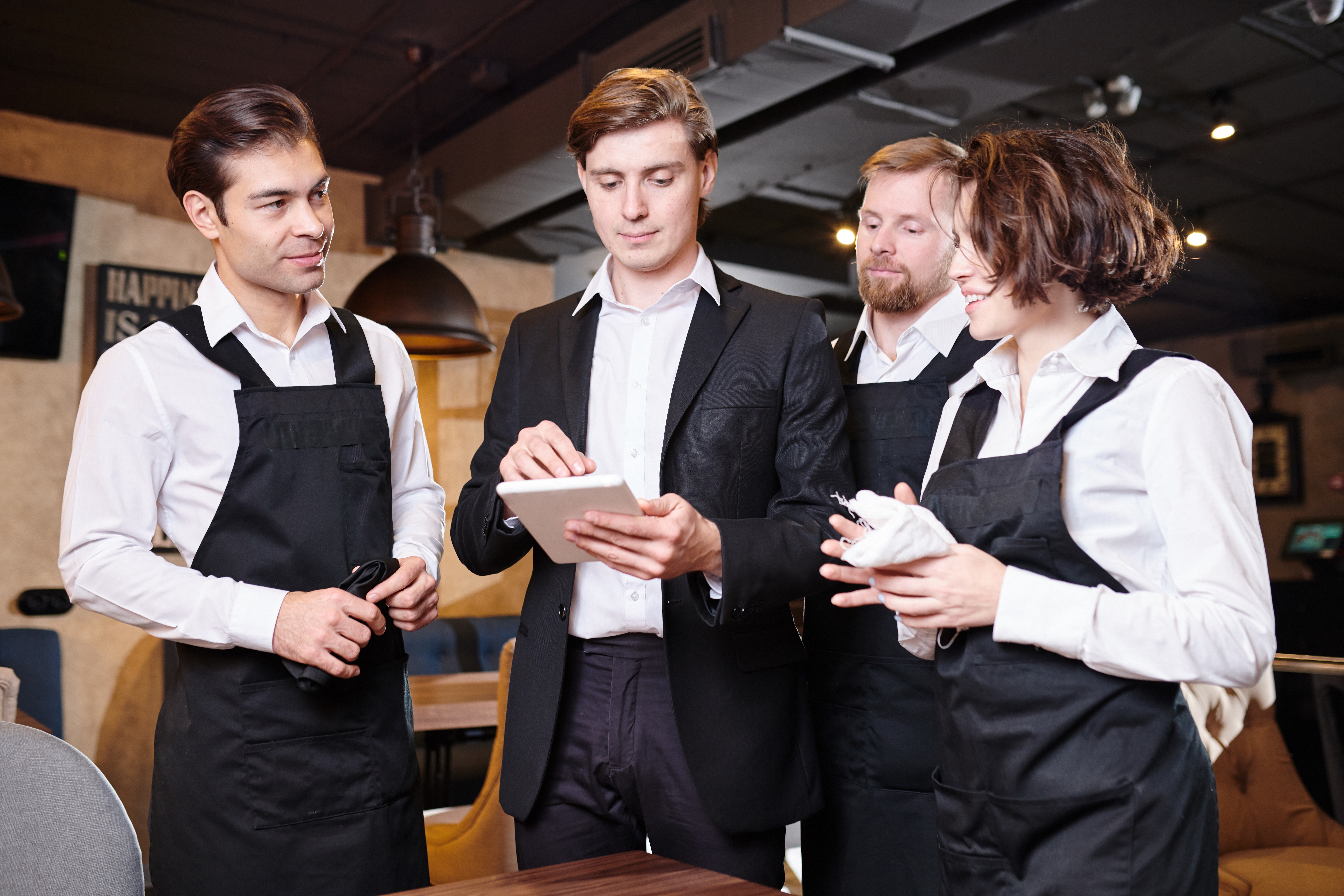 Restaurant manager dividing responsibilities with waiters using tablet in modern establishment