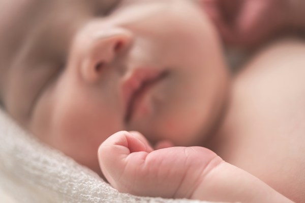 Sleeping newborn baby with tiny hand resting on soft blanket, illustrating newborn care.