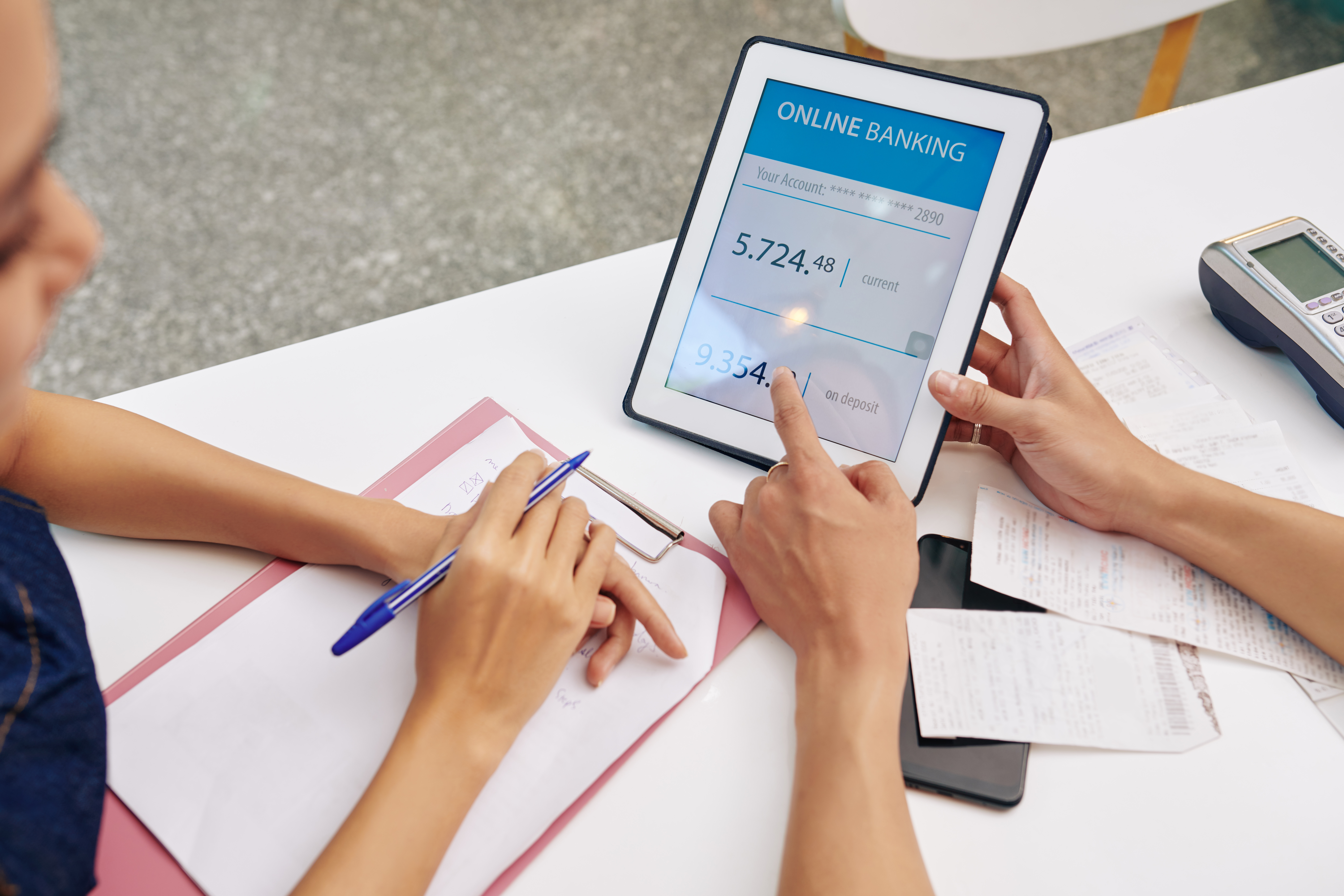 Small business owners reviewing bank account balance on tablet computer discussing debt elimination strategies.