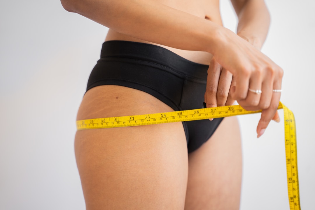Woman measuring hips with tape measure, postpartum body changes and dietary supplements.