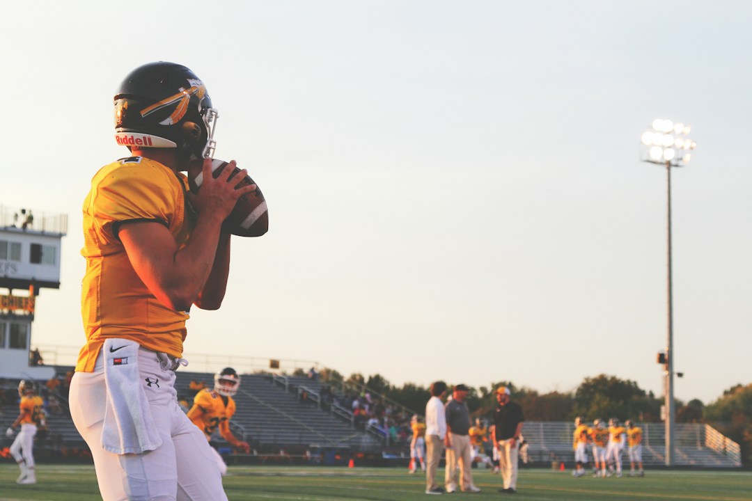 Football player in yellow uniform practicing on field, high school football program infrastructure
