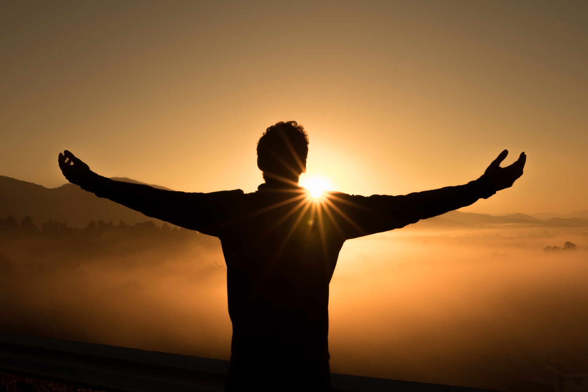 Silhouette of a person with arms outstretched against a sunset, representing spiritual connection and open mind.