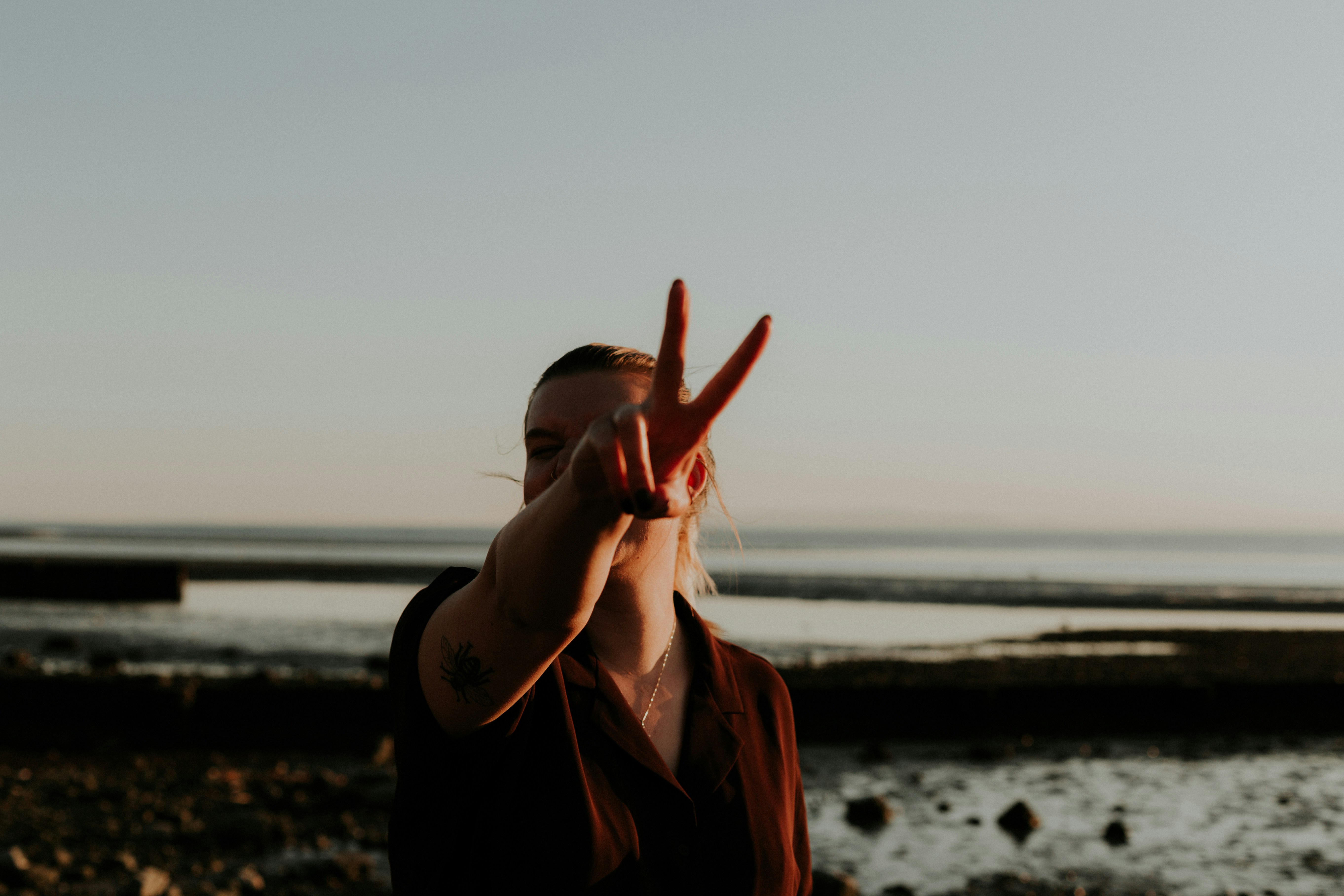 Person gesturing peace sign against ocean backdrop symbolizing strength and a positive future.