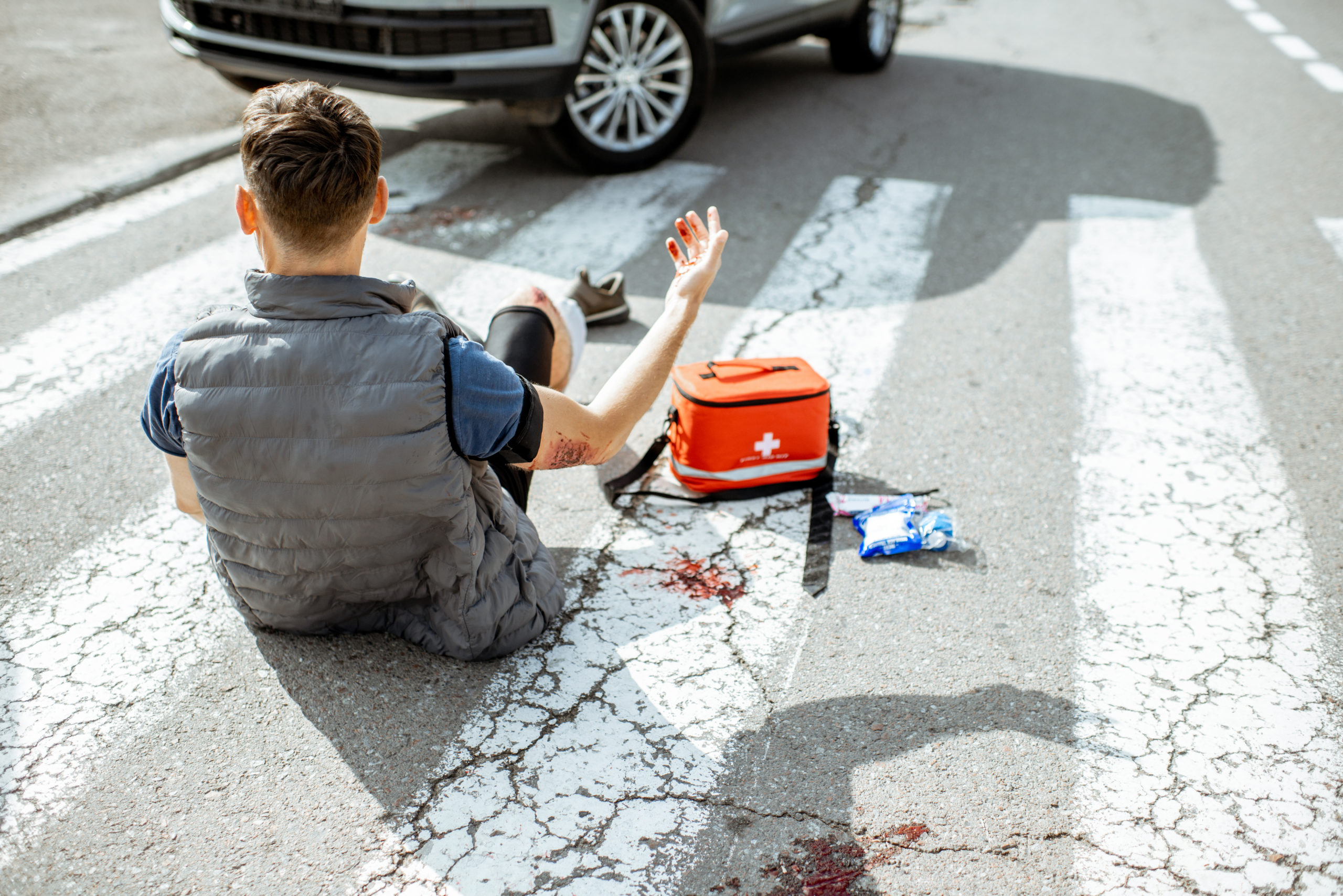 Injured man on pedestrian crossing after car accident, first aid kit nearby