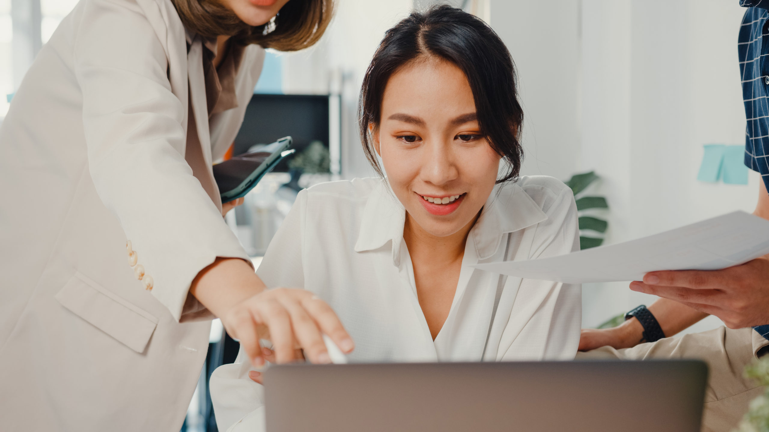 Businesswoman receiving coaching and guidance from manager at desk with laptop and paperwork.