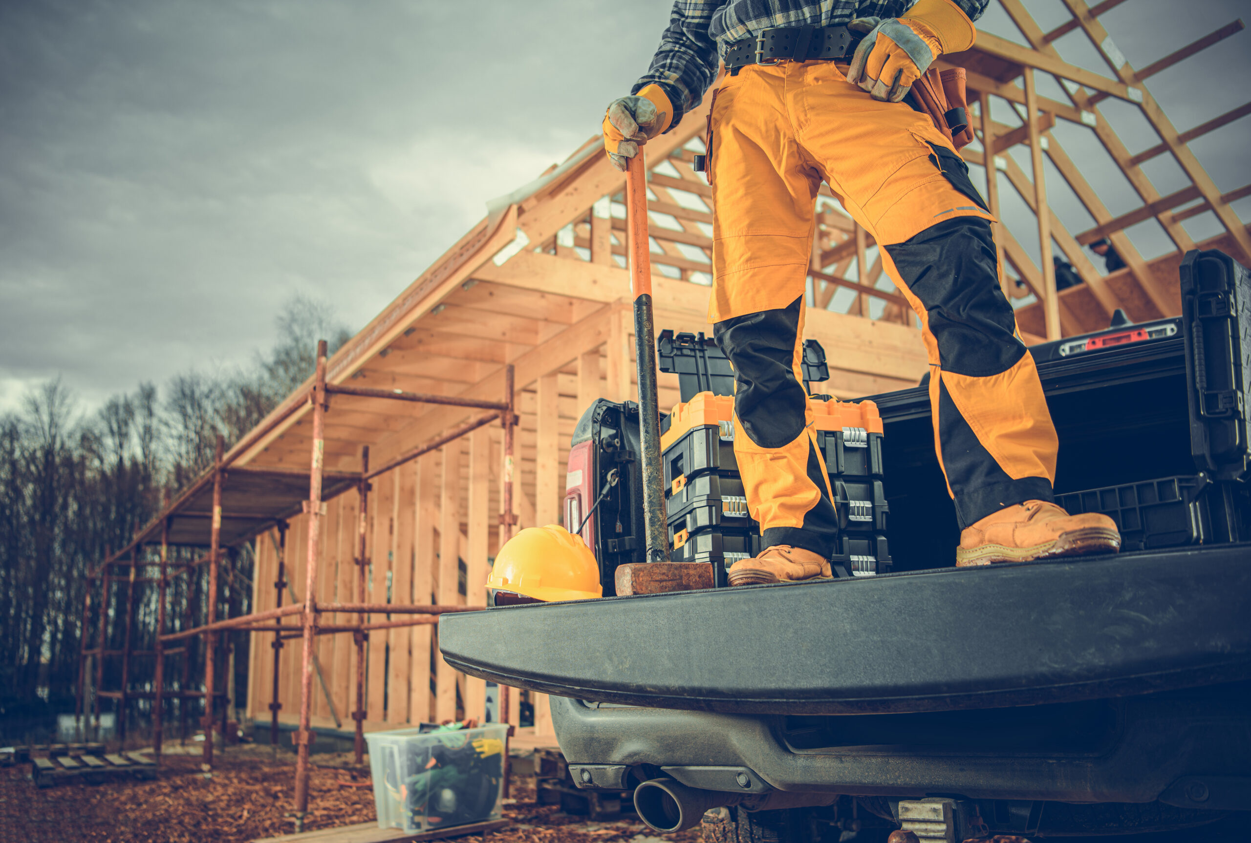 Contractor worker on pickup truck bed at wooden house construction site and building exterior.