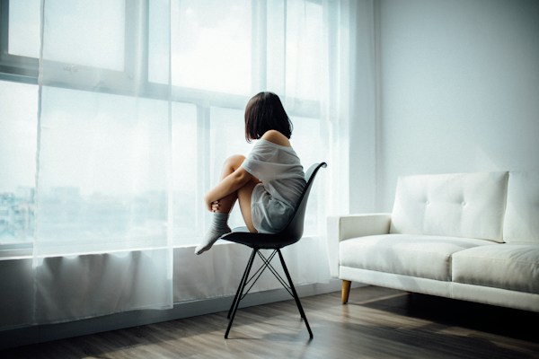 Person sitting in chair near window, reflecting on mental health and emotional well-being.